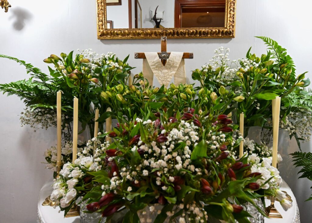 A decorated cross during the May 2025 fiestas Flower-decorated Santa Cruz displayed indoors with greenery and white blossoms for the 2025 May Fiestas