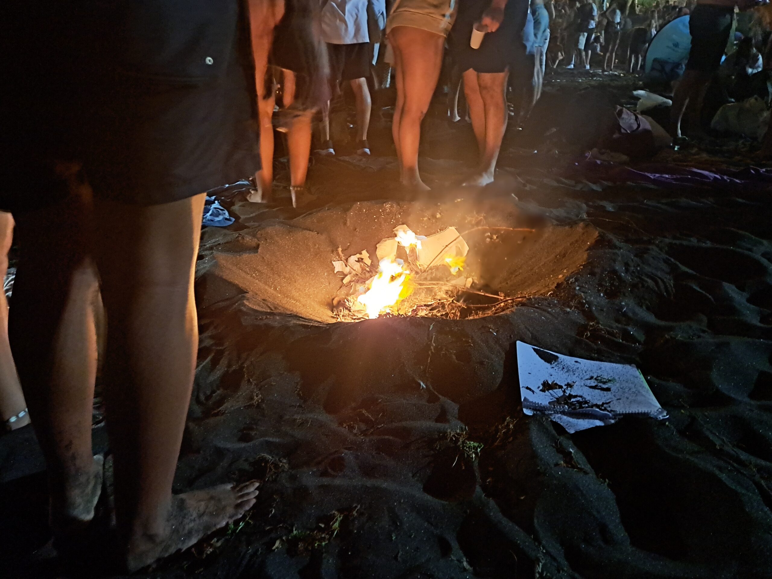 San Juan night beside the sea in Puerto de la Cruz, June 2024. Photo: PuertoDeLaCruz.info archive. Small San Juan bonfire on dark sand with people standing around it in Puerto de la Cruz