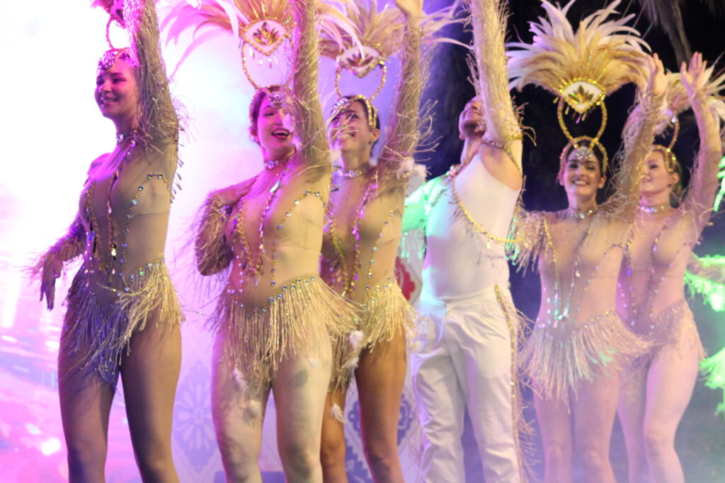 Costumed dancers in gold feathered outfits performing onstage at Summer Carnival 2025